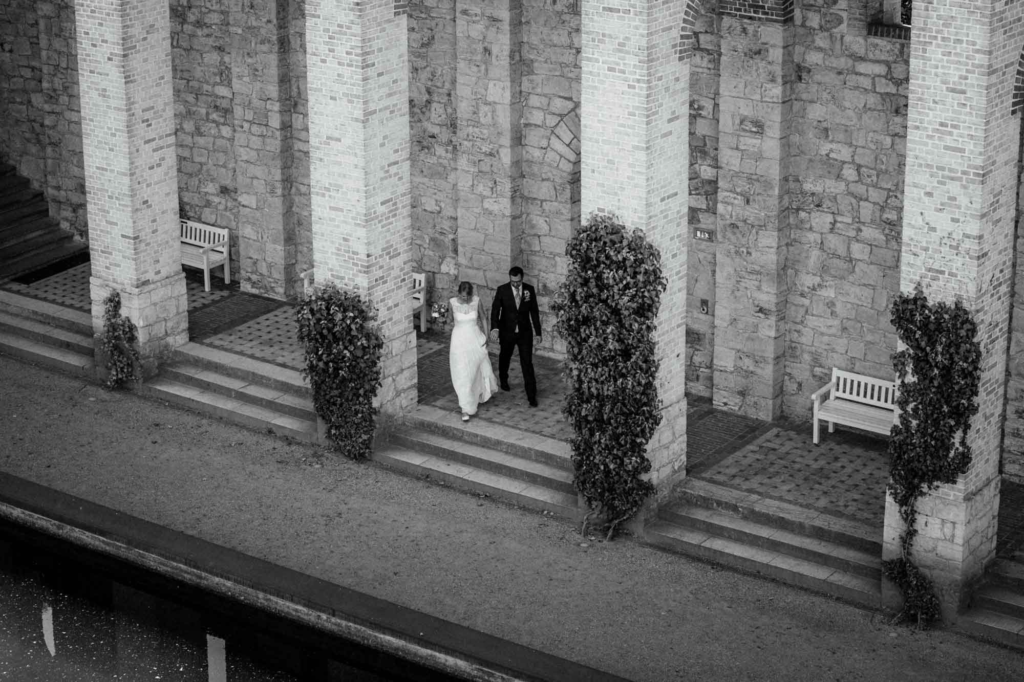 Brautpaar geht Hand in Hand einen Säulengang entlang. Schwarz-weiß Aufnahme